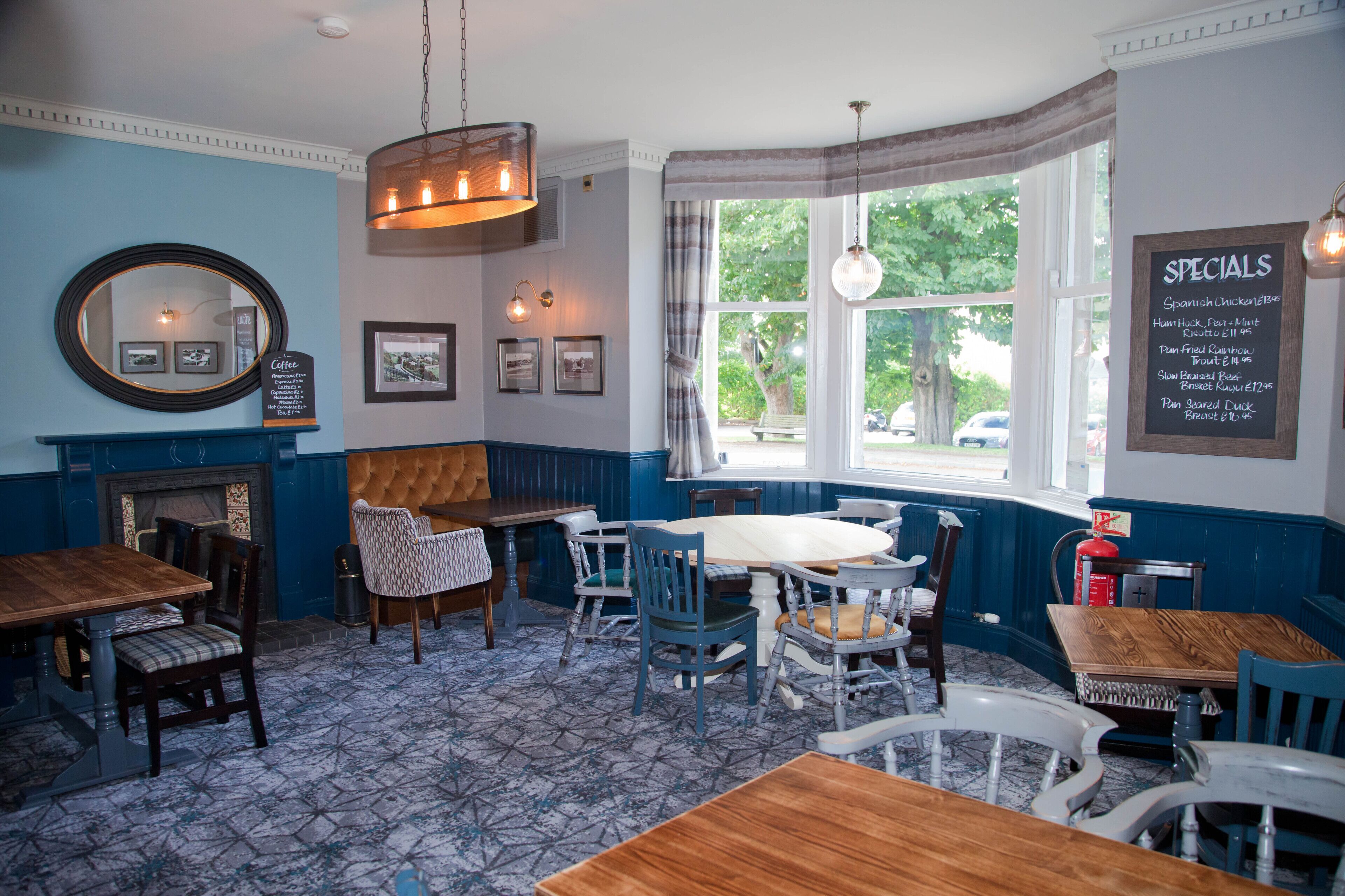 Een gezellig restaurantinterieur met houten tafels en stoelen, een open haard, ingekaderde foto's aan de muur, en een raam met uitzicht.