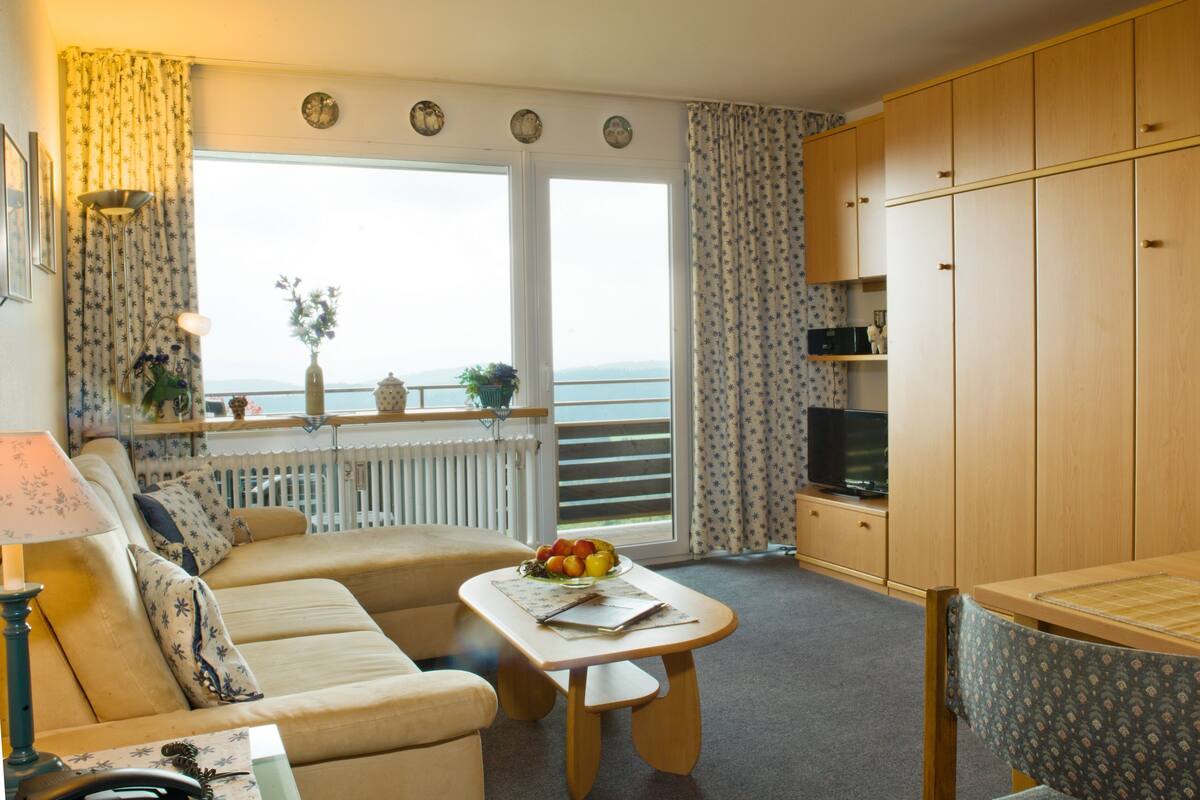 A cozy living room with a sofa, a small table with a fruit bowl, a television, and wooden cabinets.