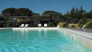 A clear swimming pool with lounge chairs and a covered seating area.