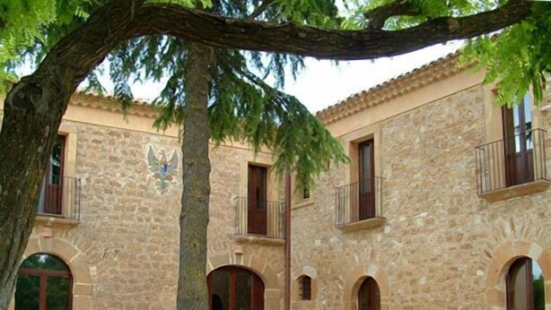 A stone building with multiple arches and balconies, surrounded by potted plants and flowers.