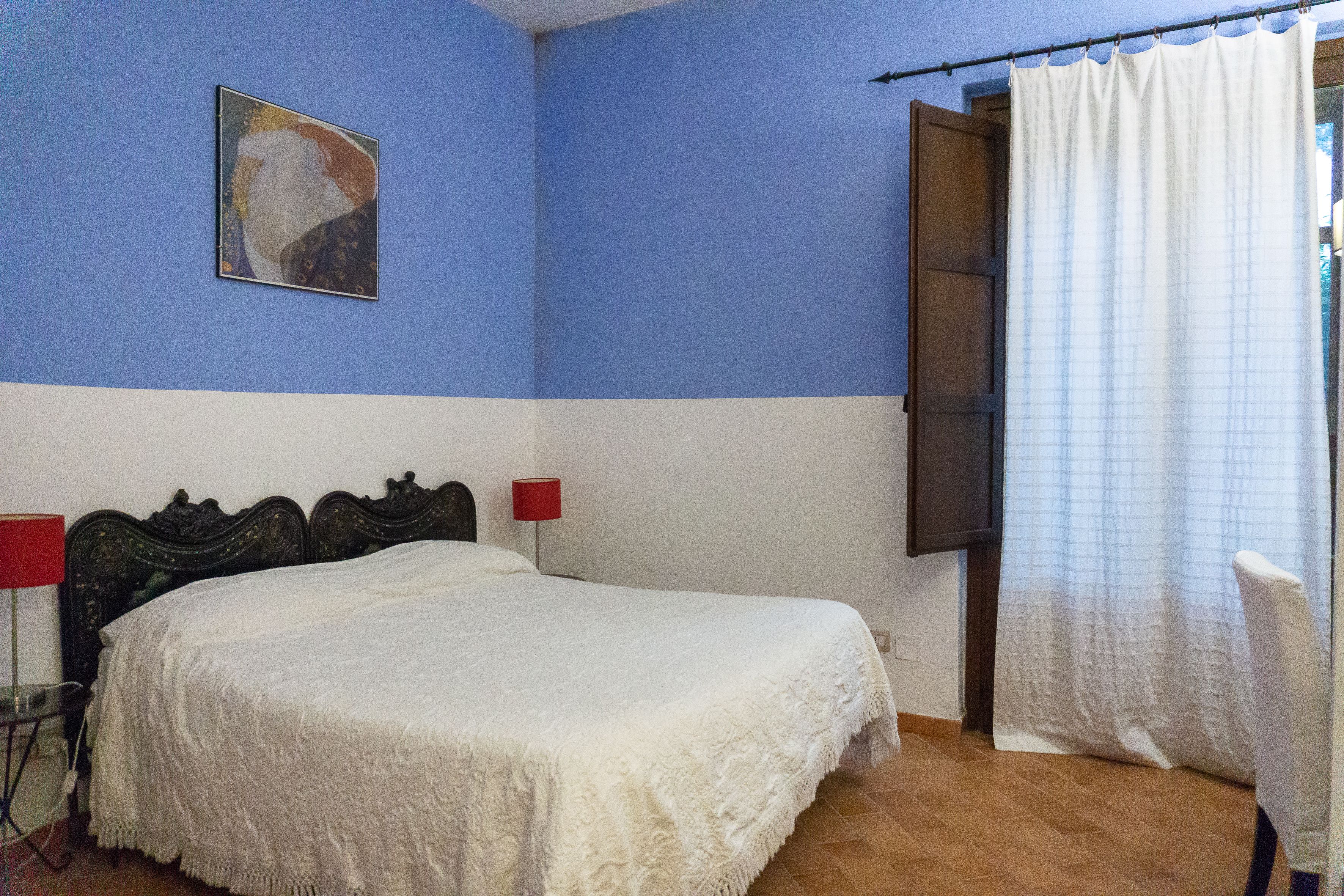 A bedroom with a bed, a red lamp, and a painting on the wall.
