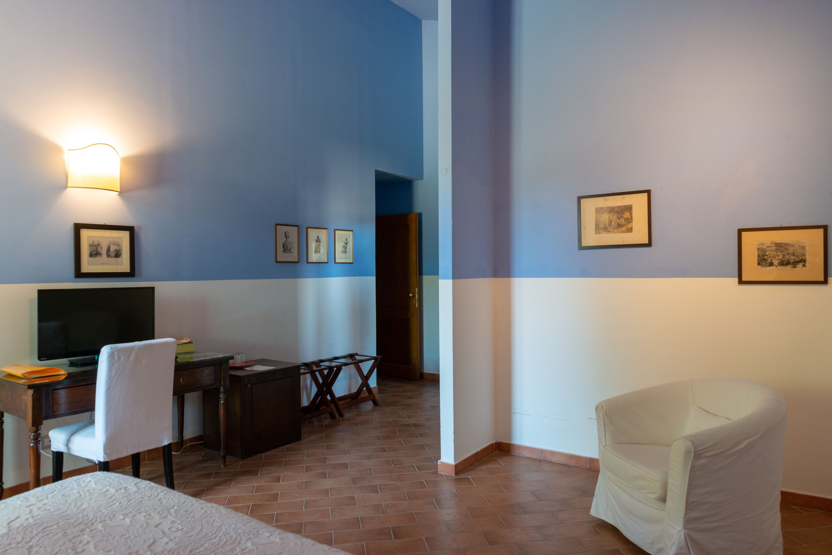 A room with a desk, chair, and television. There are framed pictures on the wall.