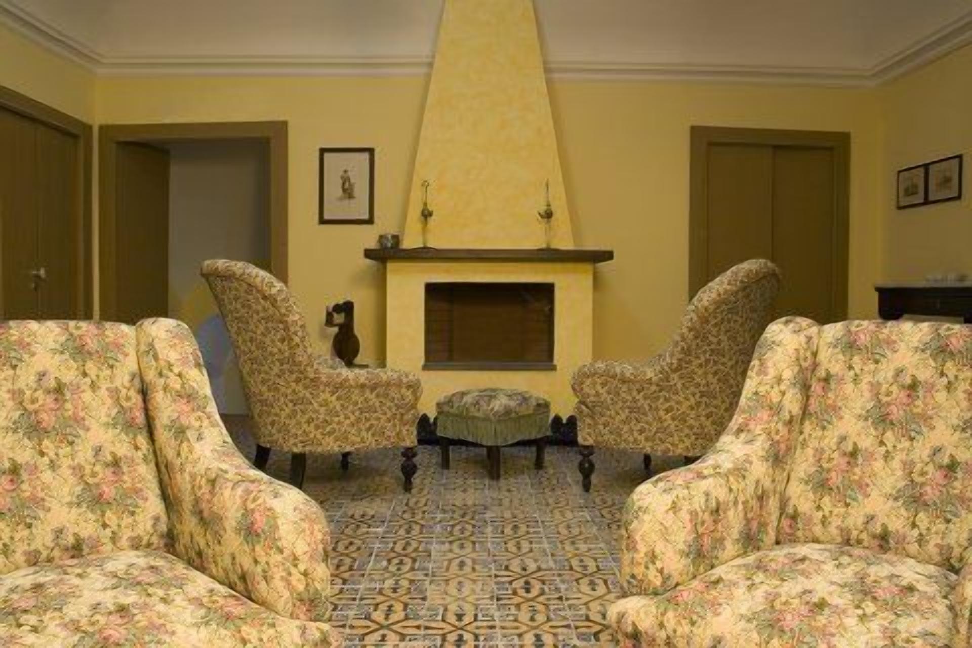 Una habitación con dos sillones tapizados con motivos florales frente a una chimenea sobre un suelo de baldosas.