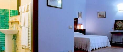 Quarto de hotel com cama, mesa de cabeceira, luminária na parede e quadro emoldurado.