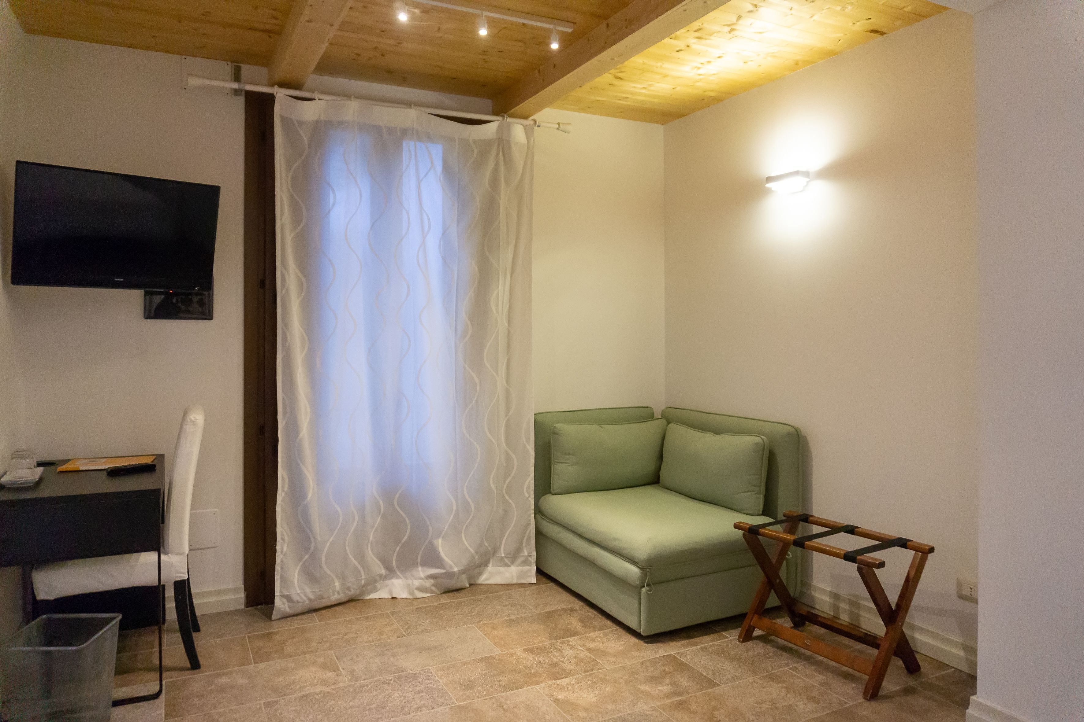 A small room with a green sofa, a wooden table, a TV mounted on the wall, and a curtain.