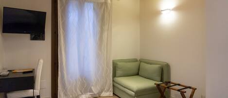 A small room with a green sofa, a wooden table, a TV mounted on the wall, and a curtain.