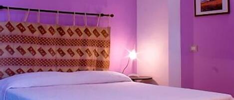 Una habitación con cama, mesita de noche y lámpara en la pared.