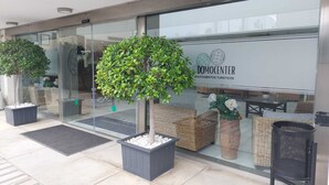 Un bâtiment moderne doté d’un espace d’accueil, de plantes en pot, de meubles en osier et d’une enseigne indiquant « DOMOCENTER APARTAMENTOS TURISTICOS ».