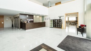 Un hall d’hôtel moderne comprenant un comptoir d’accueil, un espace salon et un escalier.