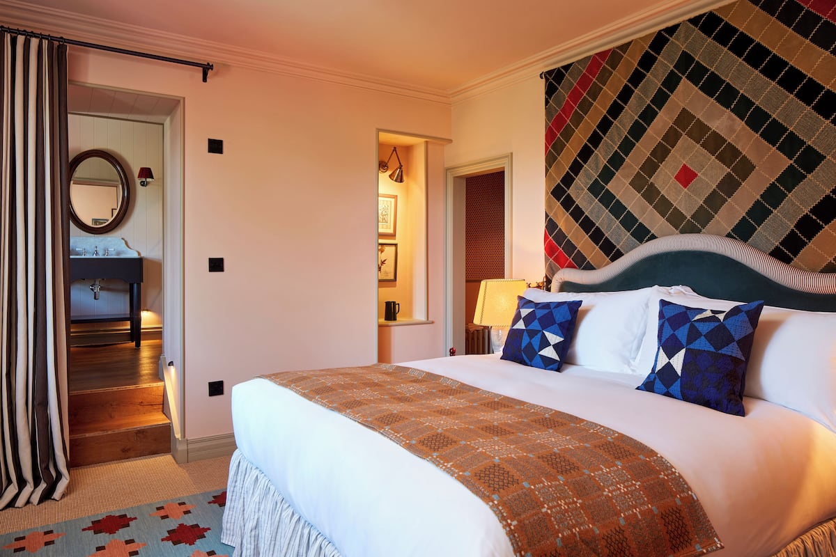 Una habitación de hotel con una cama grande, un baño con lavamanos y espejo, y un papel tapiz estampado.