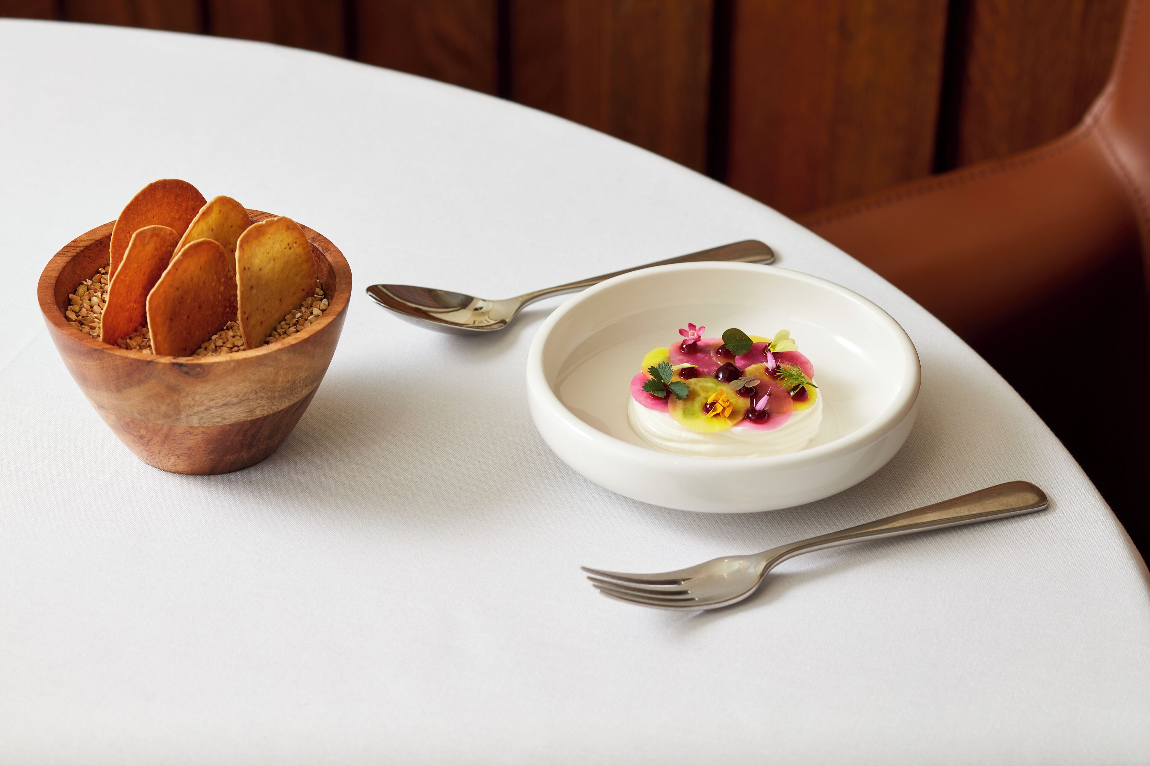 Un cuenco de madera con palitos de pan y un cuenco blanco con un postre sobre una mesa blanca.
