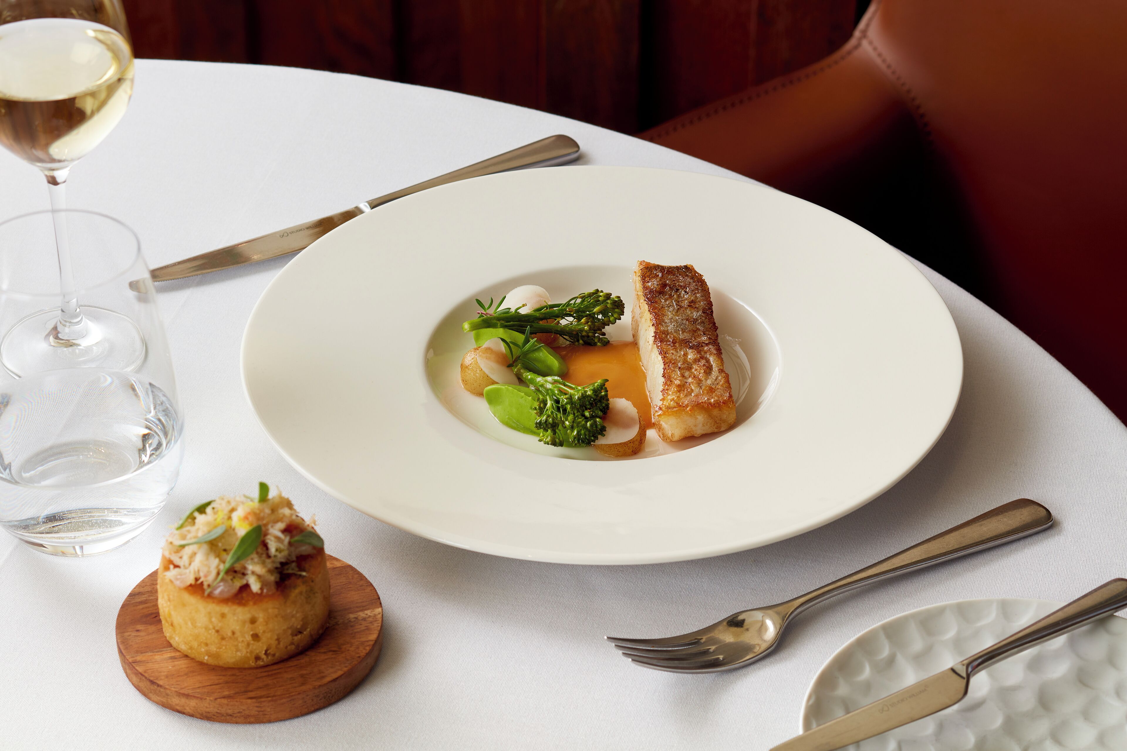 A white plate with a piece of fish, broccoli, and a small mound of food on a wooden board.