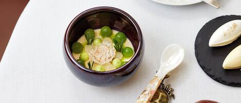 A bowl of soup with green vegetables and a decorative spoon on a white tablecloth.
