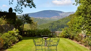 A garden with a table and chairs, a stone wall, and a mountain in the background. - Penmaenuchaf Hotel (Dolgellau)
