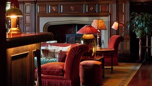 A cozy living room with a fireplace, plush red armchairs, a wooden coffee table, and a floor lamp. - Penmaenuchaf Hotel (Dolgellau)