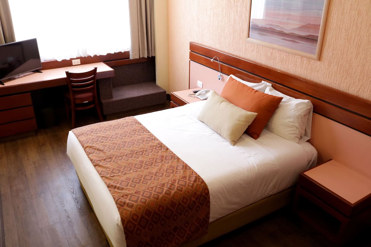 Une chambre d’hôtel avec un grand lit, un bureau avec une chaise, un téléphone et une fenêtre avec des rideaux.