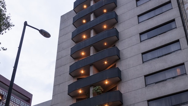 A hotel with a modern design, featuring multiple balconies with plants, a prominent entrance, and a visible restaurant sign.
