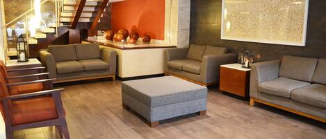 A modern living room with a sofa set, ottoman, and a decorative wall panel.