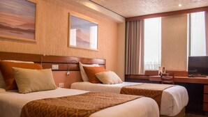A hotel room with two beds, a desk, a chair, and a TV.