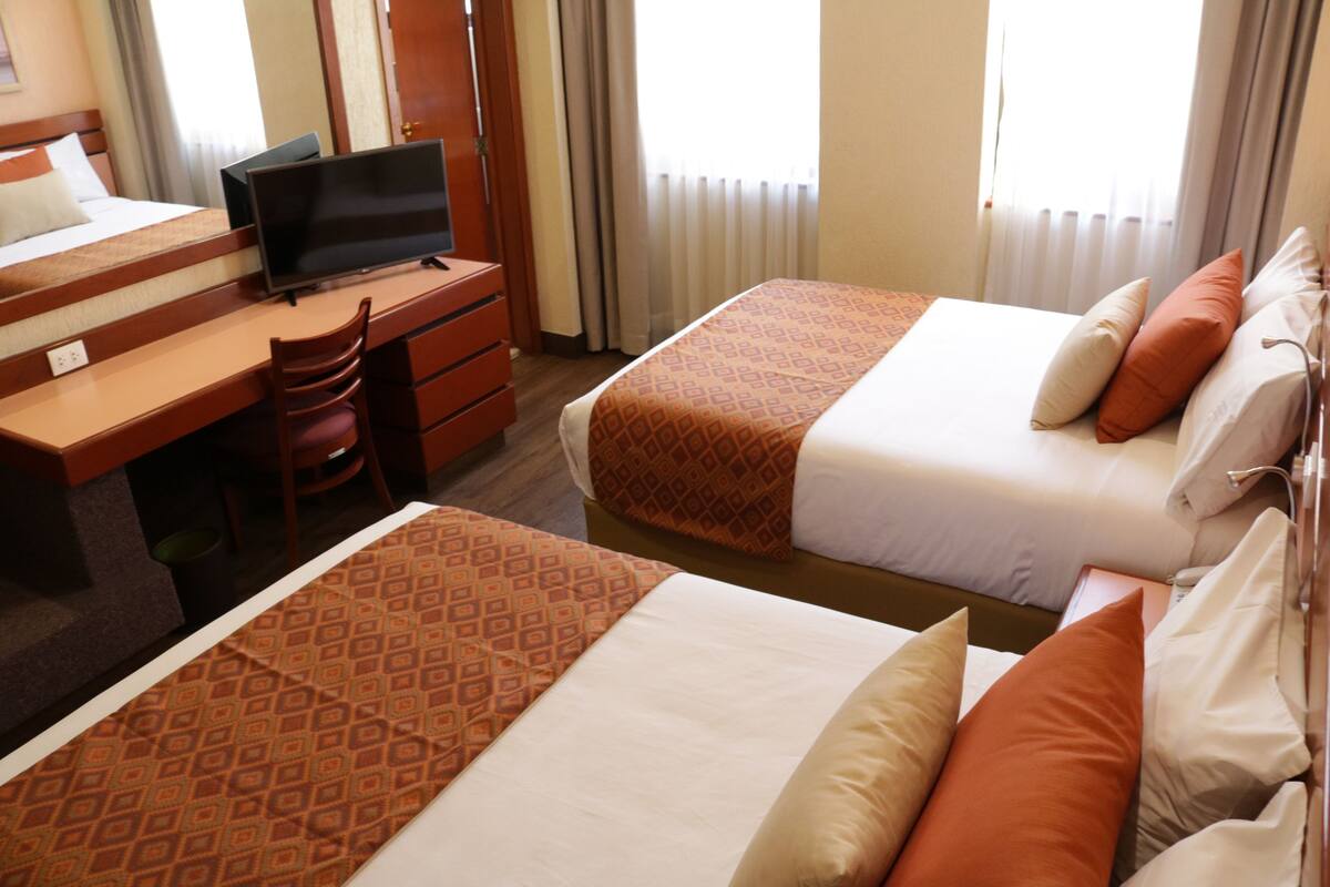 Une chambre d’hôtel avec deux lits, un bureau avec une télévision et une chaise.