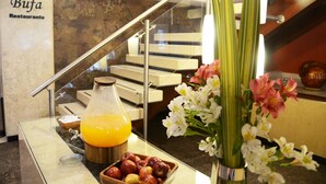 A breakfast bar with a glass of orange juice, a bowl of fruit, and a vase of flowers.