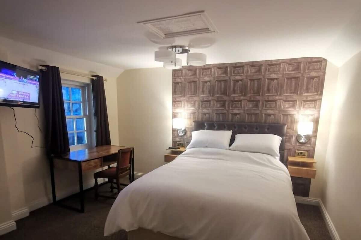 A hotel room with a bed, desk, chair, TV, and a patterned wall.