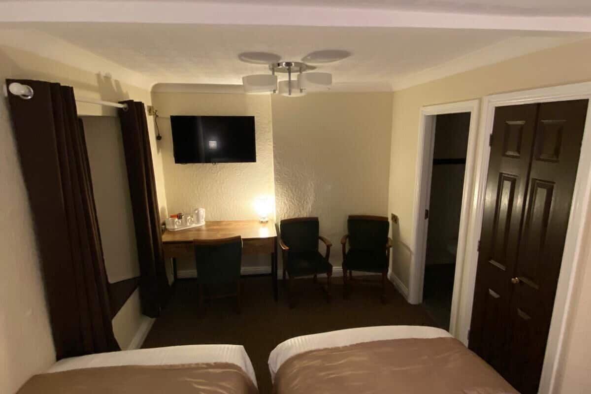 A hotel room with two beds, a desk with a chair, a television, and a ceiling fan.