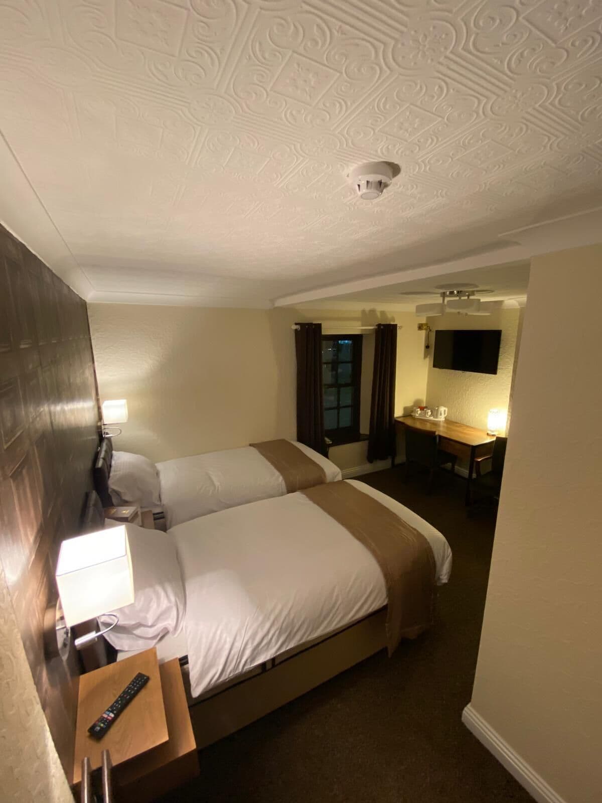 A hotel room with two beds, a desk, a TV, and a bathroom visible through an open door.