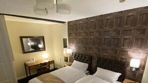 Una camera d'albergo con due letti, una testiera in legno, una piccola scrivania con una lampada e uno specchio a parete.