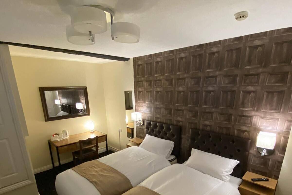A hotel room with two beds, a wooden headboard, a small desk with a lamp, and a mirror on the wall.