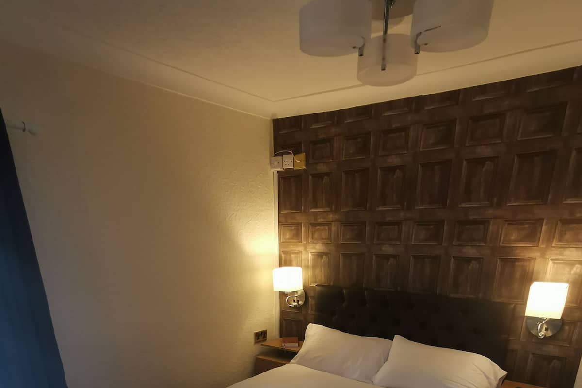 A hotel room with a large bed, two bedside tables, a wooden headboard, and two wall-mounted lamps.
