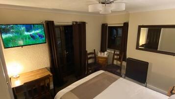 Una habitación de hotel con una cama, un escritorio con lámpara, televisión, una silla y un espejo.