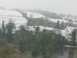 Un edificio histórico de piedra con múltiples torres, rodeado de campos y árboles cubiertos de nieve.