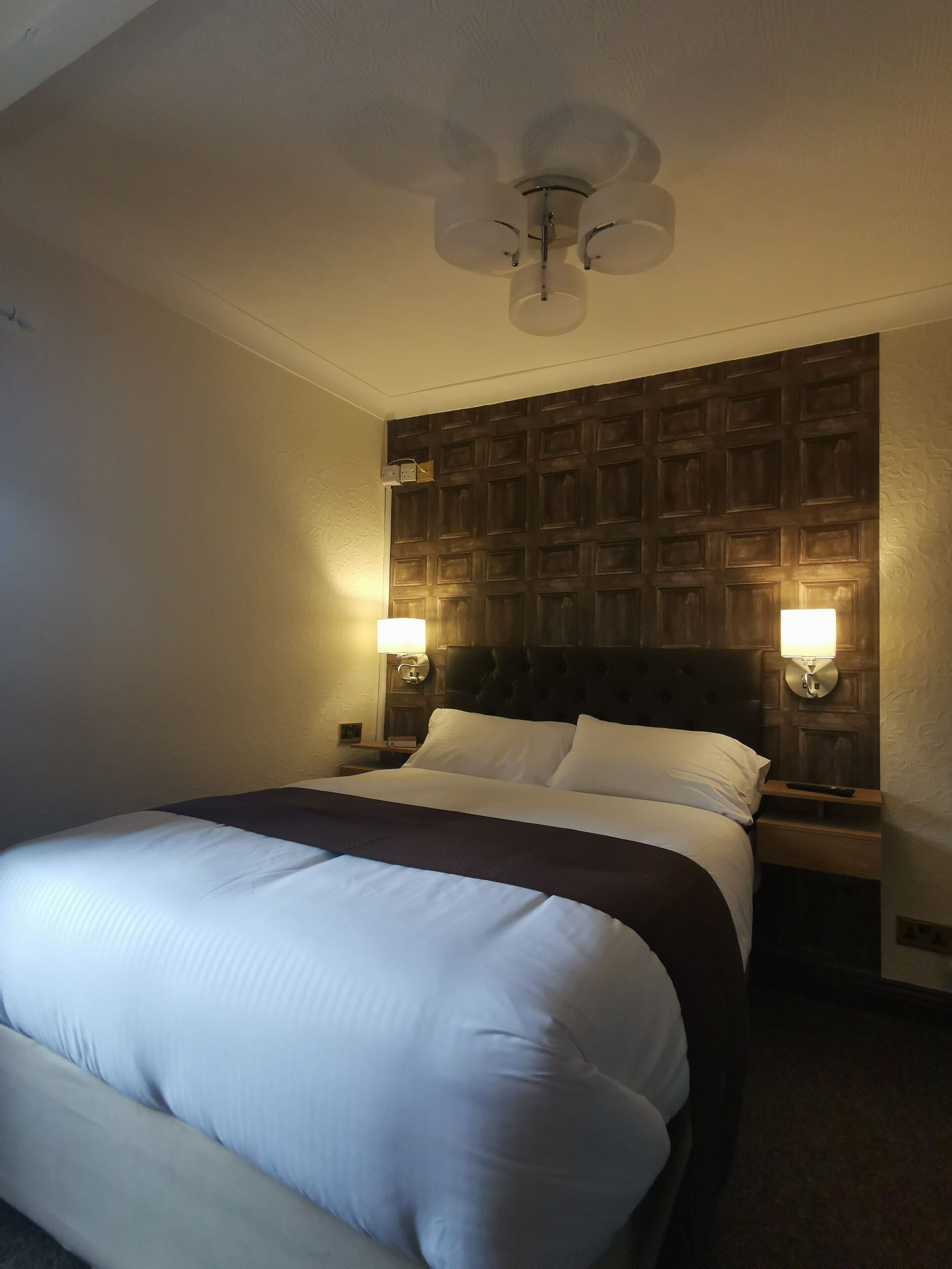 Una camera d'albergo con un letto grande, una testiera in legno, due abat-jour e un ventilatore a soffitto.