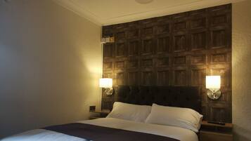Una habitación de hotel con una cama grande, cabecera de madera, dos lámparas de noche y un ventilador de techo.