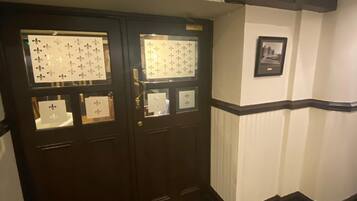 A hallway with a dark wooden door featuring two glass panels with fleur-de-lis patterns. A framed picture is mounted on the adjacent wall.