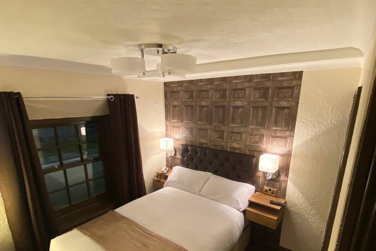 A hotel room with a large bed, two bedside tables with lamps, a ceiling fan, and a window with curtains.