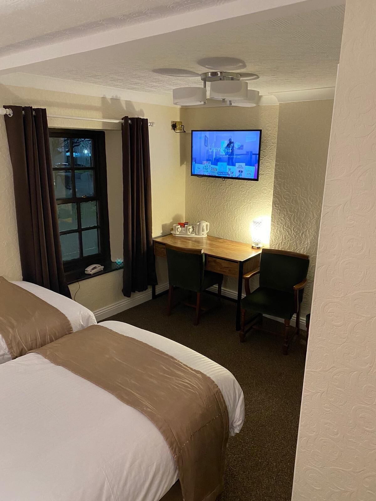 Habitación de hotel con dos camas, un escritorio con silla, televisor montado en la pared y una ventana con cortinas.