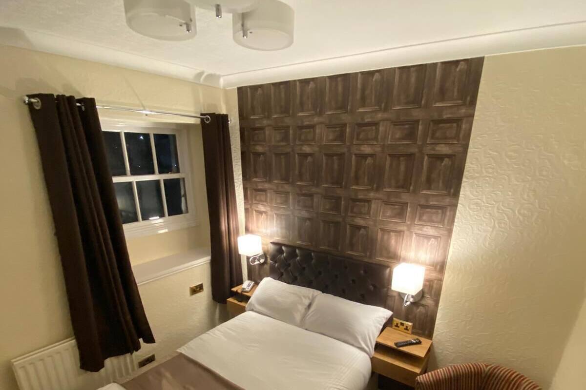 A hotel room with a bed, a nightstand, a chair, a window with curtains, and a wall with a textured pattern.