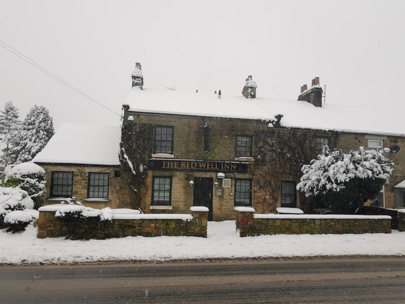 En traditionel bygning i sten med skilt der siger "The Red Well Inn".