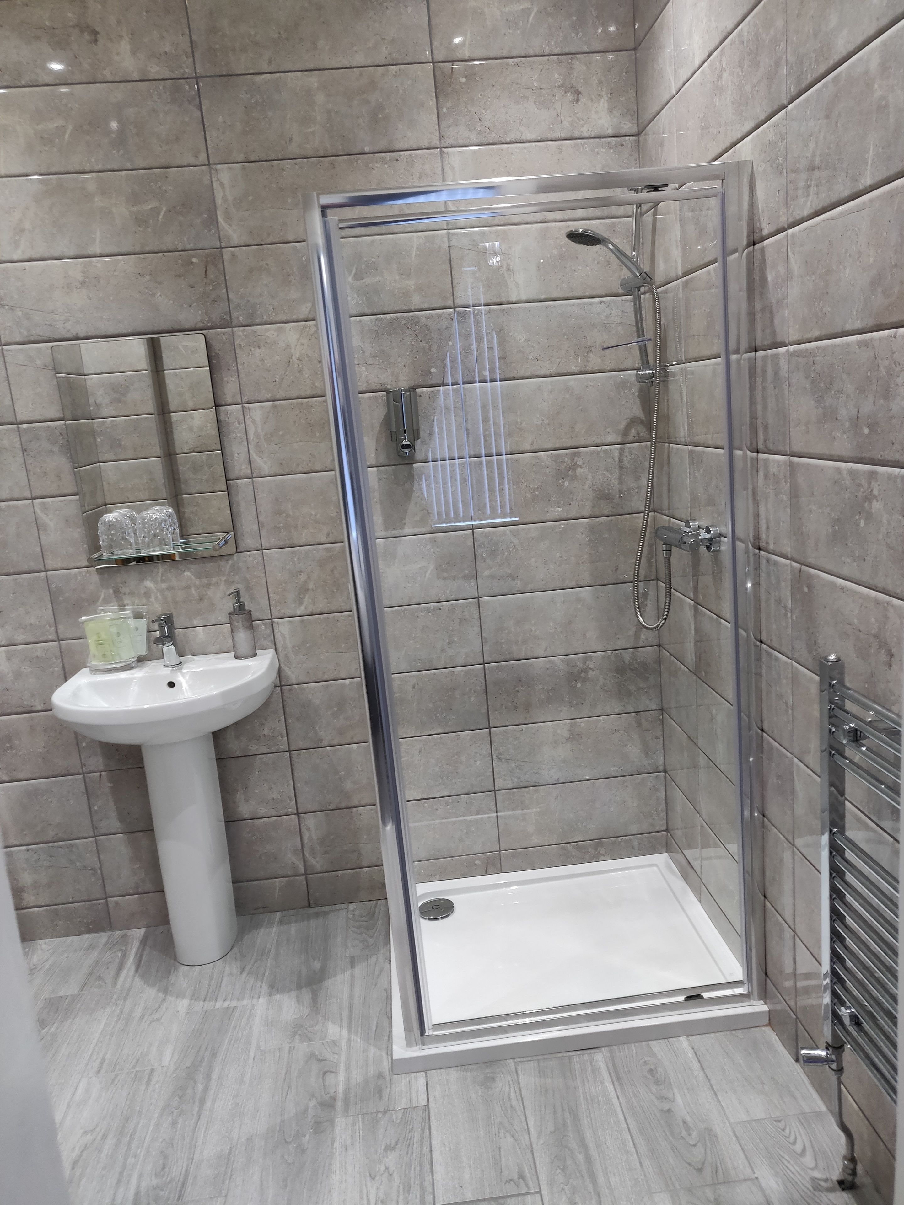 A modern bathroom with a glass shower enclosure, a pedestal sink, and a mirror.