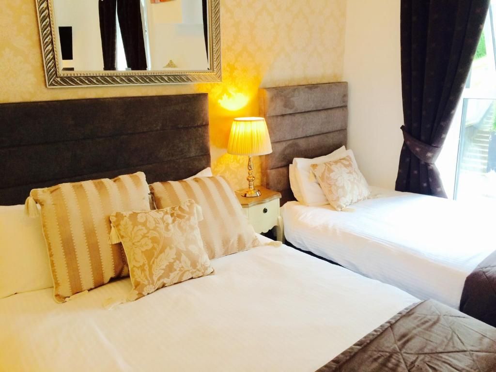 Une chambre d’hôtel avec deux lits, une table de chevet avec une lampe, un miroir et une fenêtre avec des rideaux.