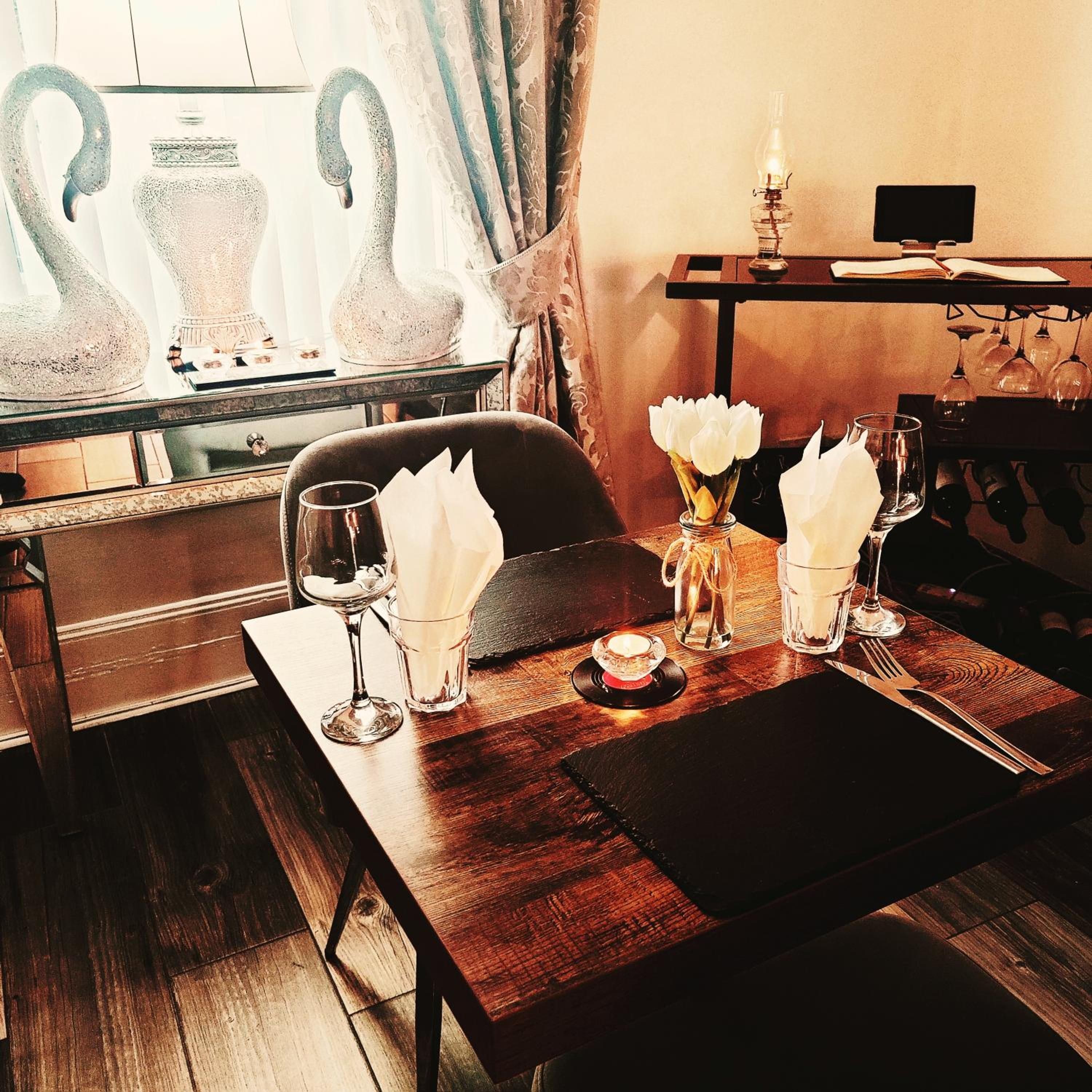 Une table à manger dressée avec des verres, une bougie et un vase rempli de fleurs.