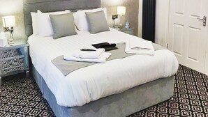 A neatly made bed with a grey headboard, a bedside table with a lamp, and a patterned floor. - Serendipity House (Londonderry)