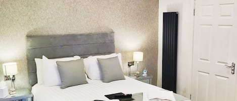A neatly made bed with a grey headboard, a bedside table with a lamp, and a patterned floor.