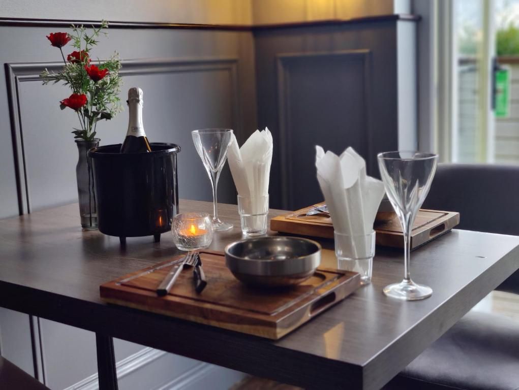 A dining table with a bottle, glasses, a candle, and a bowl on a wooden tray.