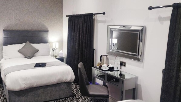 Ein Hotelzimmer mit einem Bett, einem Schreibtisch mit Spiegel, einem Sessel und einem Nachttisch mit Lampe.
