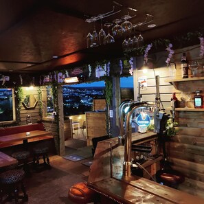 A cozy bar area with wooden furniture, a Guinness tap, and a view of the city at dusk.