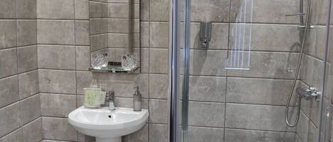 Un baño moderno con ducha de vidrio, lavamanos pedestal y un espejo sobre el lavamanos.