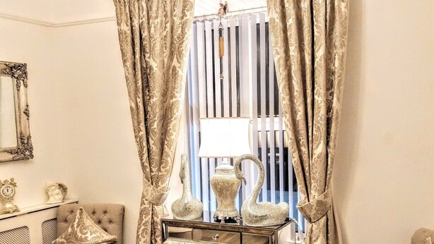 A room with a classic design, featuring a tufted armchair, a small round table, a vintage-style lamp, and a decorative vase on a console table. - Serendipity House (Londonderry)